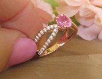 Shimmering oval pink sapphire ring with diamond-adorned split shank in rose gold.